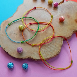 May include: A set of colorful string bracelets with colorful, sparkly beads on a wooden surface.