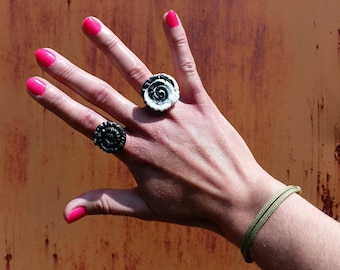 May include: A hand wearing two rings, one black and one white, with a green bracelet on the wrist.