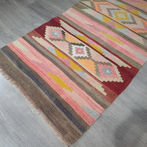 May include: A colorful, striped rug with a geometric pattern in shades of red, pink, yellow, blue, and brown. The rug has a fringed edge.