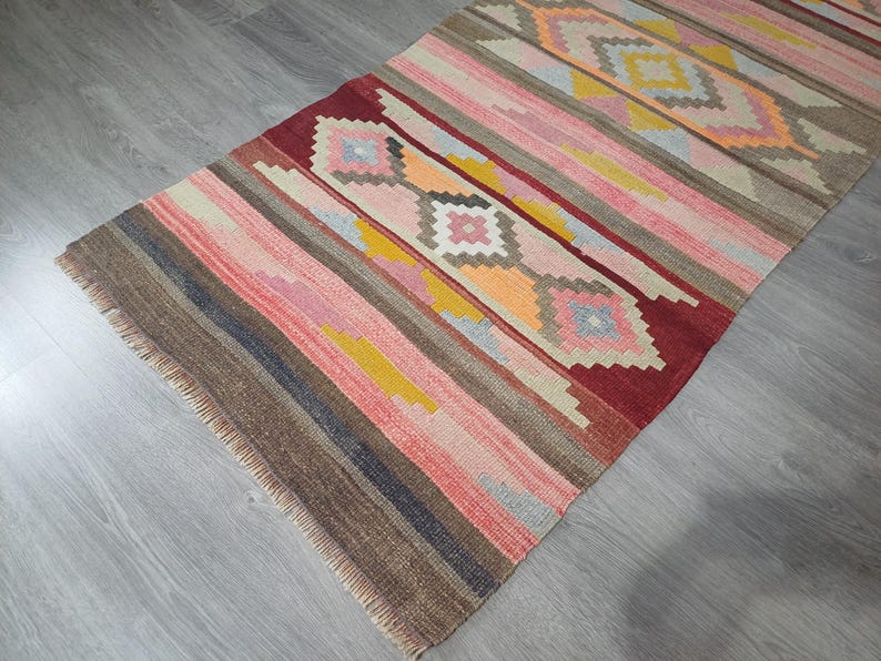 May include: A colorful, striped rug with a geometric pattern in shades of red, pink, yellow, blue, and brown. The rug has a fringed edge.