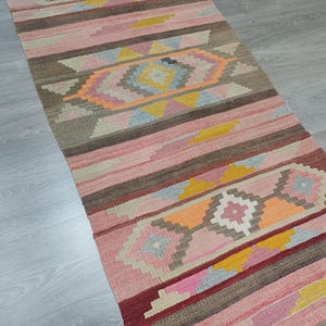 May include: A colorful, handwoven rug with a geometric pattern in shades of pink, orange, yellow, and brown. The rug has a traditional, tribal design and would add a touch of warmth and color to any room.