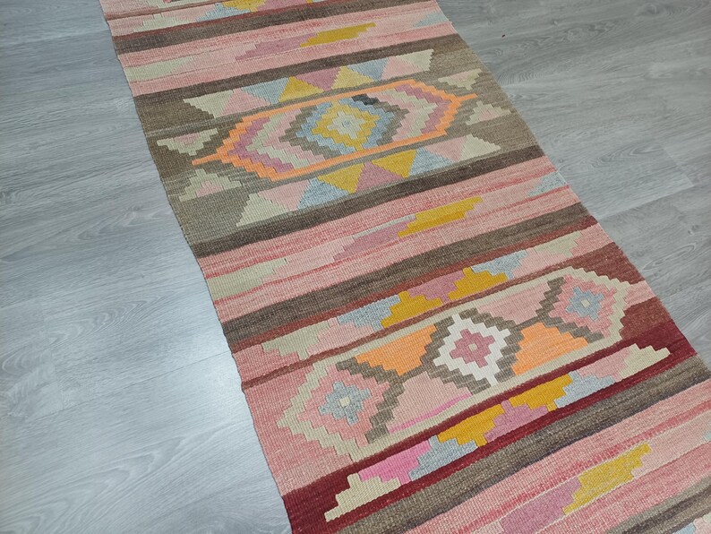 May include: A colorful, handwoven rug with a geometric pattern in shades of pink, orange, yellow, and brown. The rug has a traditional, tribal design and would add a touch of warmth and color to any room.
