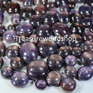 May include: A collection of purple and blue gemstone cabochons. The stones are smooth and polished, with a variety of shapes and sizes.  Treasureworldshop is printed on the image.