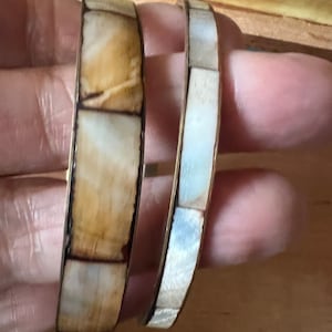 May include: Two shell bracelets, one with a white and brown shell pattern and the other with a white shell pattern.
