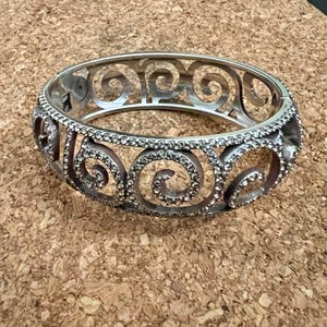 May include: A silver bangle bracelet with a swirl design and clear rhinestones.