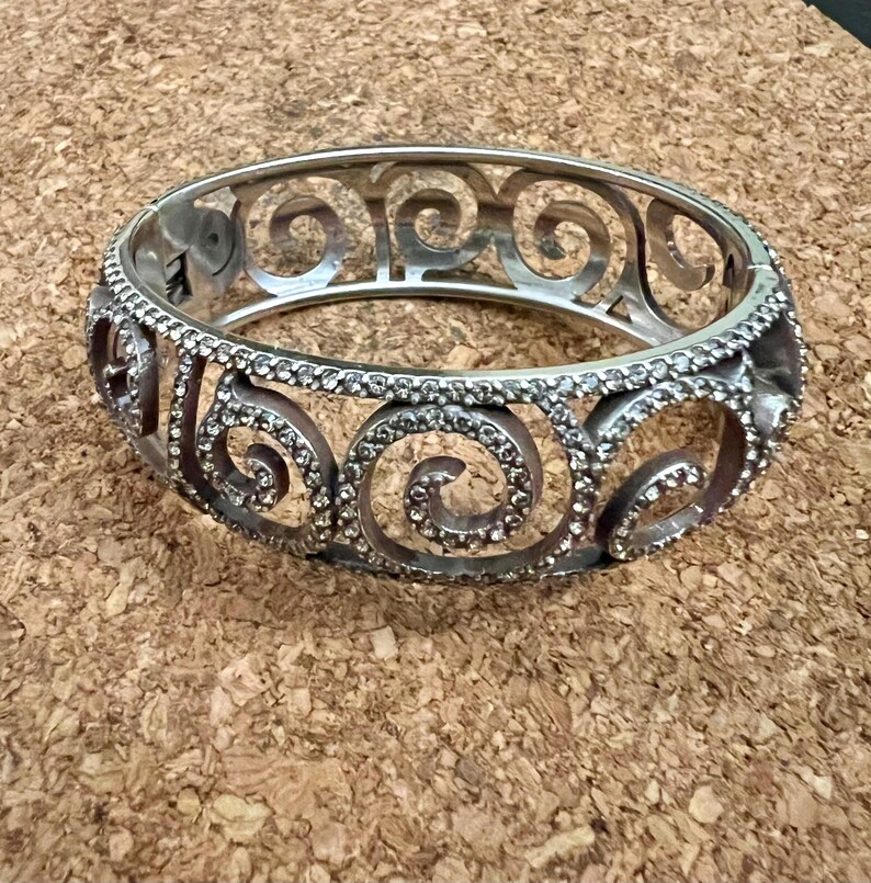 May include: A silver bangle bracelet with a swirl design and clear rhinestones.