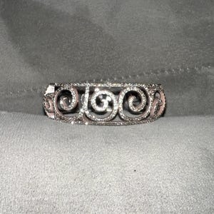 May include: A silver bracelet with a delicate, intricate design featuring a series of swirls and small clear stones.