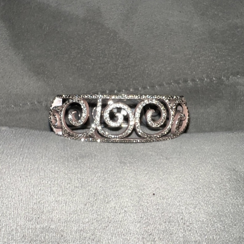 May include: A silver bracelet with a delicate, intricate design featuring a series of swirls and small clear stones.