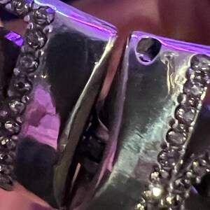 May include: A silver bracelet with a detailed design featuring a row of small black stones. The bracelet is made of multiple interlocking pieces.