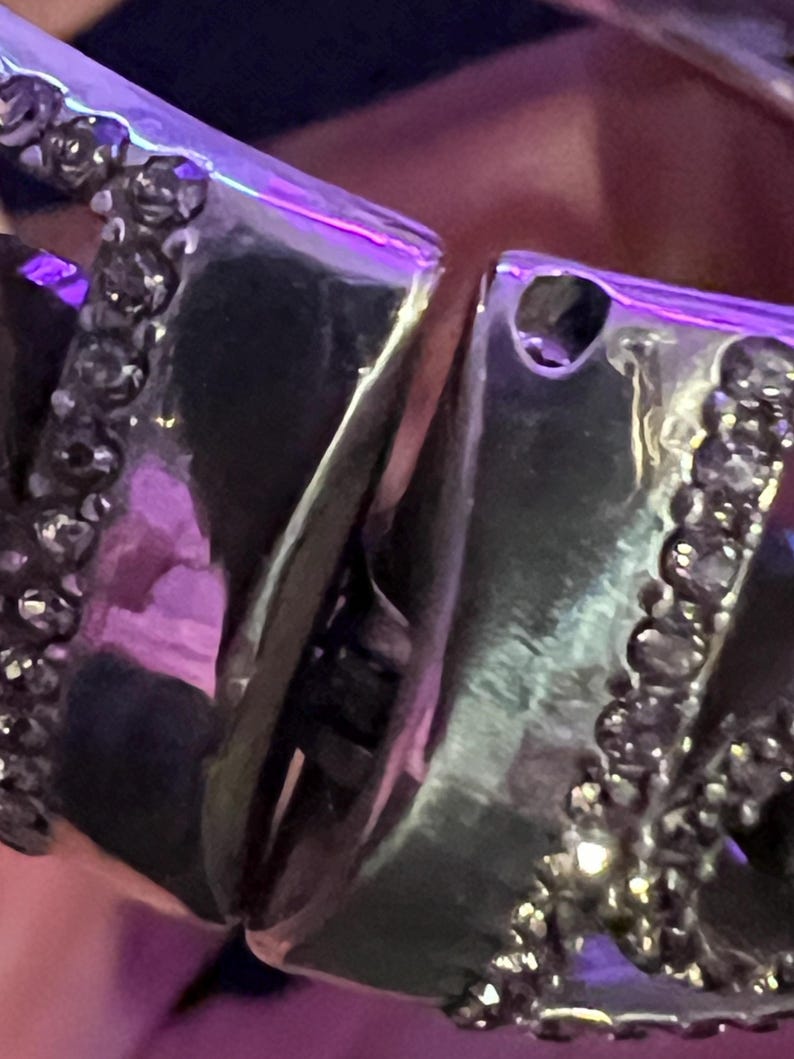 May include: A silver bracelet with a detailed design featuring a row of small black stones. The bracelet is made of multiple interlocking pieces.