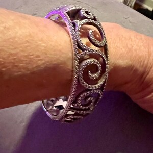 May include: A silver bangle bracelet with a swirl design and clear stones.