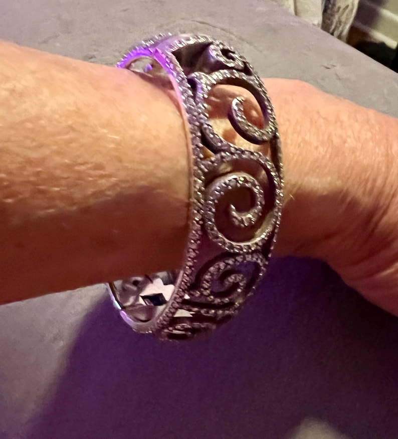 May include: A silver bangle bracelet with a swirl design and clear stones.