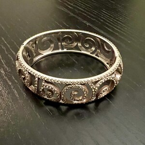 May include: A silver bangle bracelet with a swirl design and clear rhinestones.
