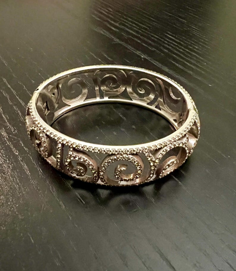 May include: A silver bangle bracelet with a swirl design and clear rhinestones.