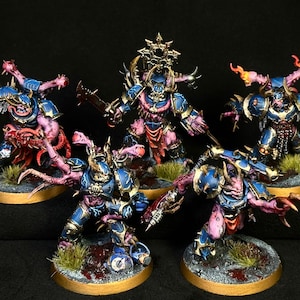Puede incluir: Un conjunto de cinco figuras en miniatura pintadas que representan guerreros blindados con placas azules y doradas, carne rosada expuesta y extremidades mutadas. Cada figura se asienta sobre una base circular con suelo texturizado.