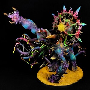 May include: A multi-limbed creature miniature featuring a vibrant purple and blue gradient skin tone, numerous tentacles with dripping yellow slime, and a large, spiked circular halo structure in shades of pink, red, and teal on its back.