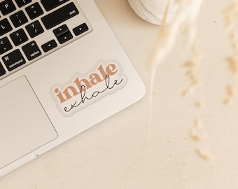 May include: A sticker with the words "inhale exhale" in a peachy-pink color with black cursive writing on a white laptop.