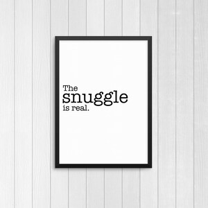 May include: Black and white typography print with the text "The snuggle is real." in a black frame.