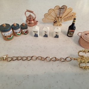 May include: A miniature kitchen set with a copper kettle, a gold peacock fan, a copper pot, a bottle of liqueur, and various miniature food containers labeled "Flour", "Sugar", "Tea", "Oatmeal", "Tea", and "Rice".