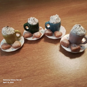 May include: Three miniature ceramic mugs with whipped cream on top, each with a small plate of heart-shaped cookies. The mugs are green, blue, and pink.