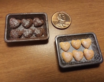 Könnte beinhalten: Zwei Mini-Backformen gefüllt mit herzförmigen Keksen. Eine Form enthält Schokoladenkekse, die mit Puderzucker bestäubt sind, die andere enthält hellbraune Kekse, die mit Puderzucker bestäubt sind.