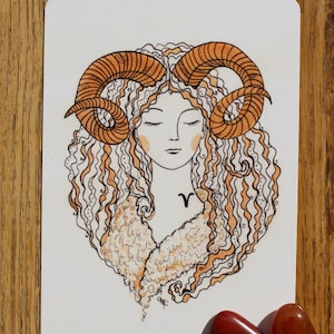 Puede incluir: Una ilustraci&oacute;n dibujada a mano de una mujer con el pelo rizado y cuernos de carnero. La mujer lleva un abrigo de piel y tiene un peque&ntilde;o s&iacute;mbolo de carnero en el pecho. La ilustraci&oacute;n est&aacute; hecha en tonos naranja y marr&oacute;n.