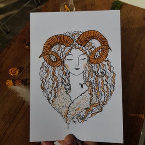 Puede incluir: Una ilustraci&oacute;n dibujada a mano de una mujer con el pelo rizado y cuernos de carnero. La mujer lleva un abrigo de piel marr&oacute;n y blanco. La ilustraci&oacute;n est&aacute; hecha con tinta negra y naranja sobre papel blanco.
