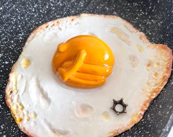 The fried egg frog, fried egg in the frying pan, egg frog, wall object, sculpture, fried egg, modeled frog, art for the kitchen