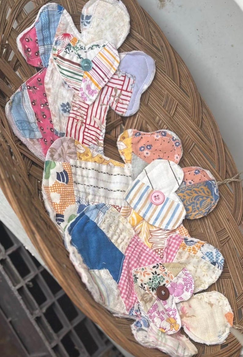 Puede incluir: Dos almohadillas de tela construidas con varios parches acolchados en colores y patrones variados, incluyendo rosa, azul, amarillo y blanco. Cada almohadilla presenta una secci&oacute;n superior en forma de coraz&oacute;n asegurada con un peque&ntilde;o bot&oacute;n de pl&aacute;stico azul, rosa o marr&oacute;n.