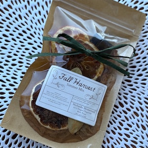 May include: A clear plastic bag filled with dried orange slices, spices, and a green ribbon. The bag is sealed with a brown paper backing and a label that reads "Fall Harvest Simmer Mix."