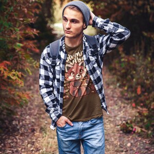 May include: A man wearing a dark chocolate brown t-shirt with a red panda graphic and the text "Autumn Vibes". He is also wearing a black and white plaid shirt, blue jeans, and a gray beanie.