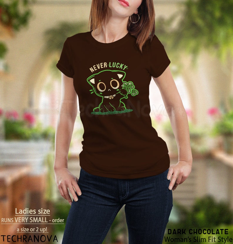 May include: A brown t-shirt with a black cat graphic holding a four-leaf clover. The text "NEVER LUCKY" is above the cat. The shirt is a women's slim fit style.