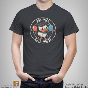 Może przedstawiać: Szary t-shirt z nadrukiem kresk&oacute;wkowego gęsi w czapce absolwenta trzymającego balony. Tekst "Qualified Silly Goose" jest nadrukowany w k&oacute;łku wok&oacute;ł gęsi.
