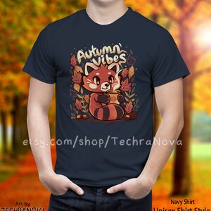 May include: A navy blue t-shirt with a red panda holding a cup of coffee. The shirt has the text "Autumn Vibes" in white lettering. The panda is surrounded by autumn leaves and acorns.