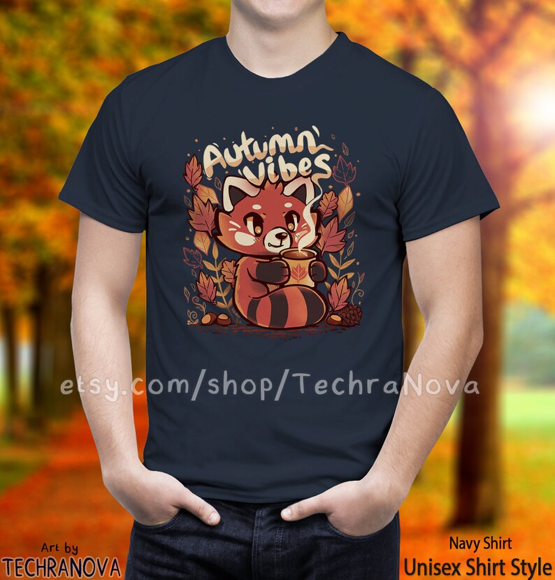 May include: A navy blue t-shirt with a red panda holding a cup of coffee. The shirt has the text "Autumn Vibes" in white lettering. The panda is surrounded by autumn leaves and acorns.