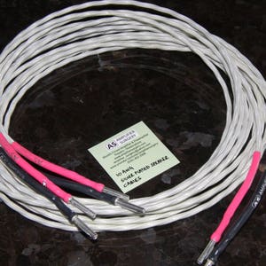 May include: Coiled silver-plated speaker cables with pink and black ends. The cables have silver connectors. A small card with text is visible.