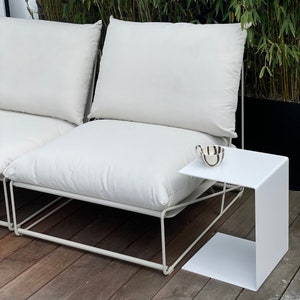Könnte beinhalten: Weißes Sofa mit Metallrahmen, zwei weißen Kissen und einem weißen Beistelltisch aus Metall mit einer weißen Keramiktasse darauf.
