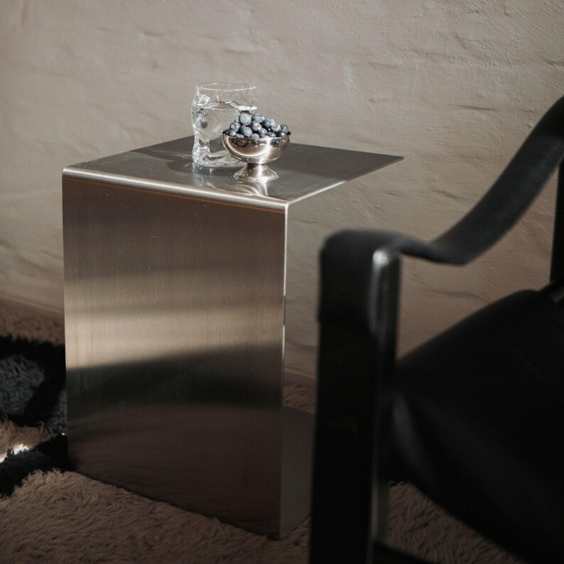 May include: A silver metal side table with a glass of water and a bowl of blueberries on top. The table is next to a black chair.