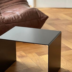 Könnte beinhalten: Ein schwarzer Metall-Beistelltisch mit rechteckiger Platte und offenen Seiten. Der Tisch steht auf einem Holzboden.