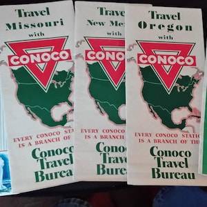 May include: A collection of vintage Conoco Travel Bureau brochures. The brochures feature state maps and travel information, with the Conoco logo prominently displayed. The color scheme includes red, green, and white. One brochure highlights Wyoming, another Missouri, New Mexico, Oregon, and the United States.