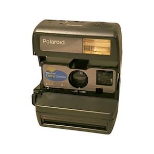 Peut inclure: Un appareil photo Polaroid OneStep Talking Camera noir avec une étiquette bleue et blanche indiquant "OneStep Talking Camera".