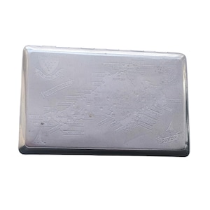 May include: A rectangular silver cigarette case with a detailed map of Cornwall and Devon, England, engraved on the lid. The case features text and illustrations, including the words "Cornwall" and "Devon."