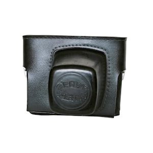 May include: Black leather camera case with a molded front section. The case is rectangular with a flap closure. The front of the case features the embossed text "SERVI".