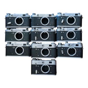 May include: A collection of ten vintage rangefinder cameras arranged in a grid. Each camera features a silver top plate, a black textured body, and a central lens mount. Several cameras display the Cyrillic text FED-2 or FED-3 on the top plate.