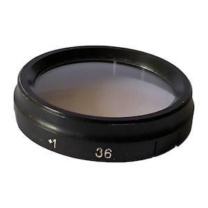 Könnte beinhalten: Schwarzer Objektivfilter mit einem klaren Glaseinsatz. Der Filter hat die Nummern "*1" und "36" auf der Seite aufgedruckt.