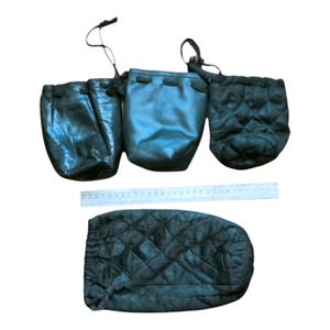 May include: Four black drawstring pouches of varying textures and shapes, including two smooth and two quilted designs, arranged with a 30 cm ruler showing scale. The pouches feature cinched tops with black cords for closure and storage.