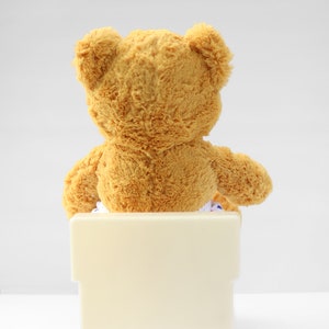 Puede incluir: Un oso de peluche marr&oacute;n sentado en un orinal blanco.