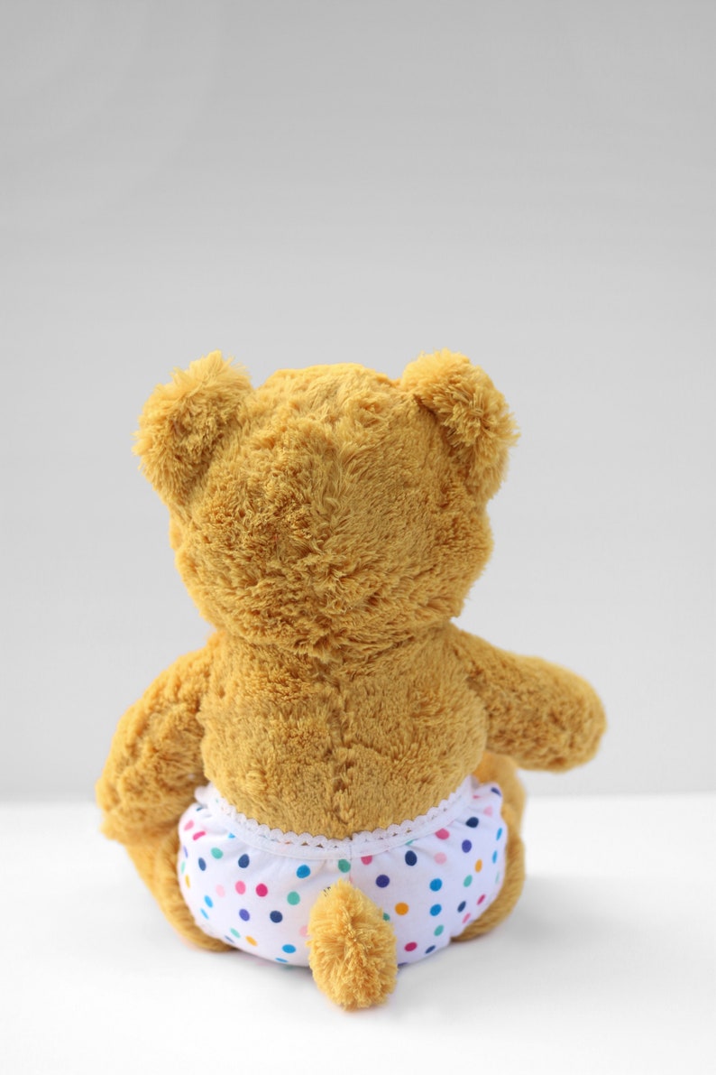 Puede incluir: Un oso de peluche marr&oacute;n que lleva un pa&ntilde;al blanco con lunares de colores.