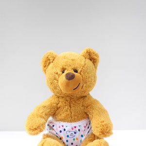 Puede incluir: Un oso de peluche marr&oacute;n que lleva ropa interior blanca con lunares de colores y un peque&ntilde;o gr&aacute;fico de cara de oso.