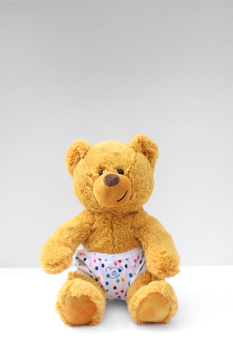 Puede incluir: Un oso de peluche marr&oacute;n que lleva ropa interior blanca con lunares de colores y un peque&ntilde;o gr&aacute;fico de cara de oso.